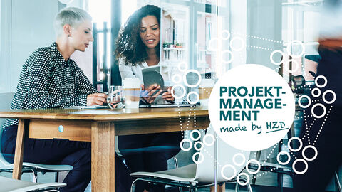 Menschen sitzen in einem Büro mit der Aufschrift: Projektmanagement made by HZD